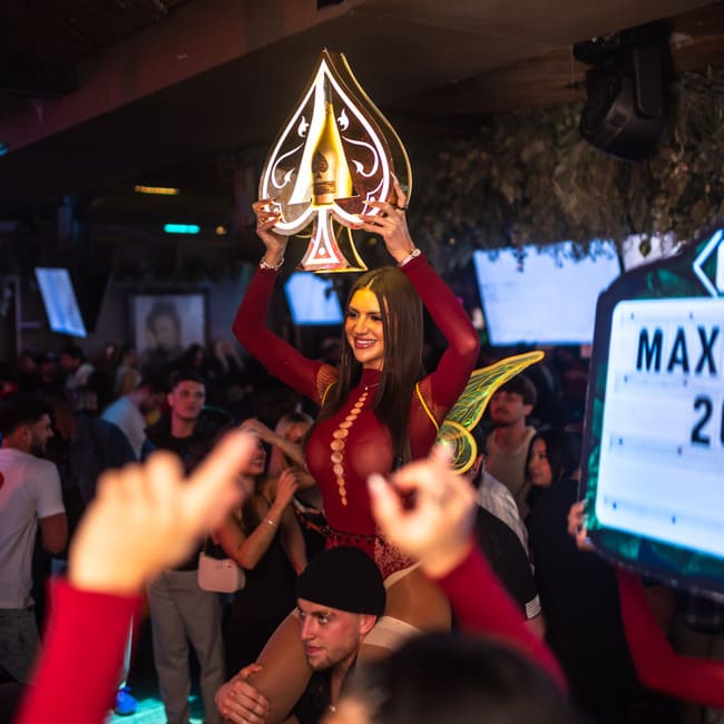 Bottle service server holding a glowing champagne sign above her head while being carried through a crowded nightclub.
