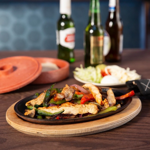 Sizzling platter of fajitas with grilled chicken strips, bell peppers, and onions, accompanied by beer and tortillas