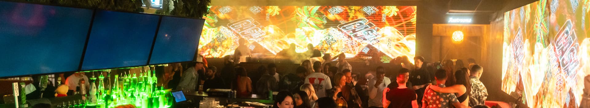 A lively nightclub with people socializing and dancing with a colorful LED screen in the background.